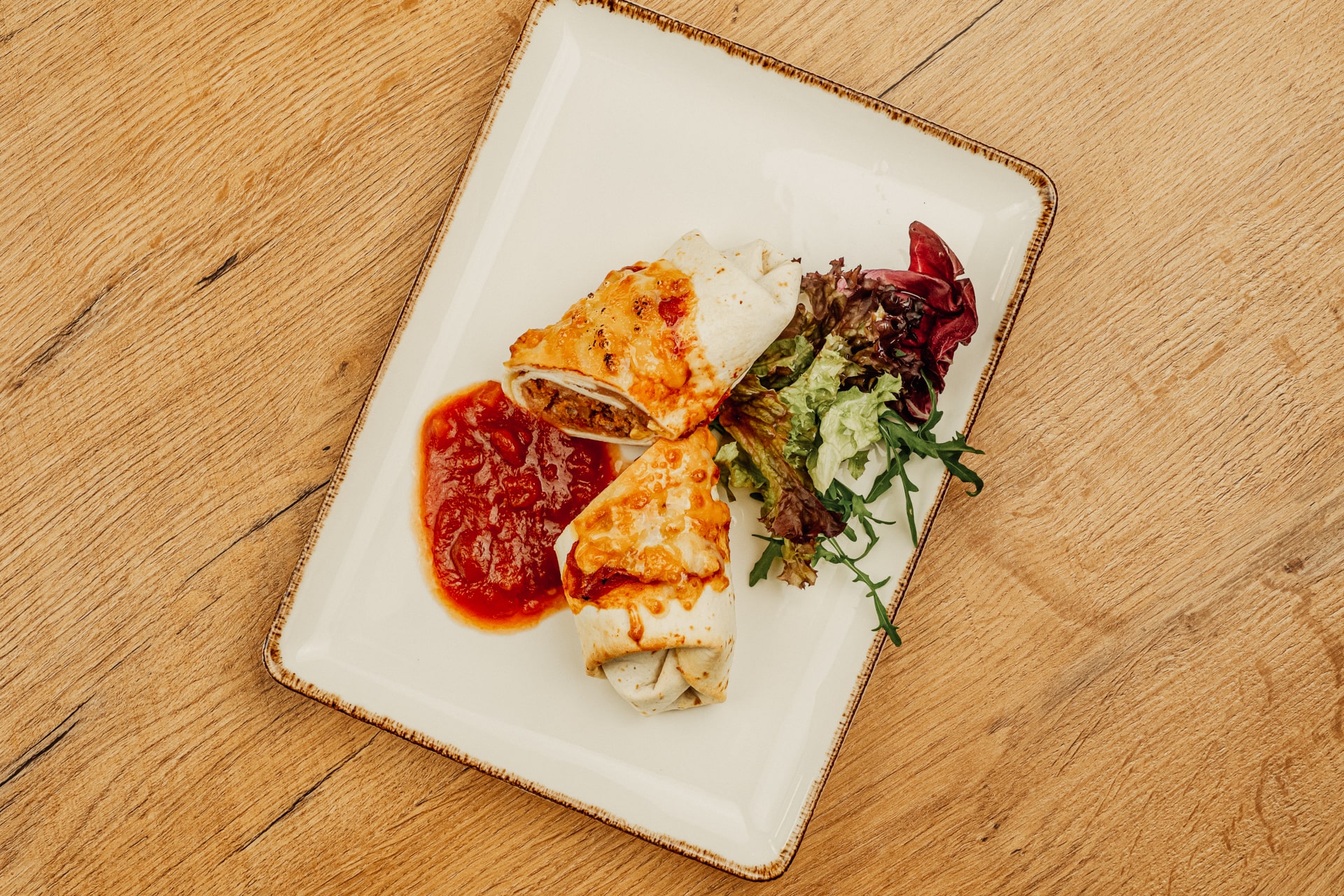 Burrito auf Sauce mit Beilagensalat