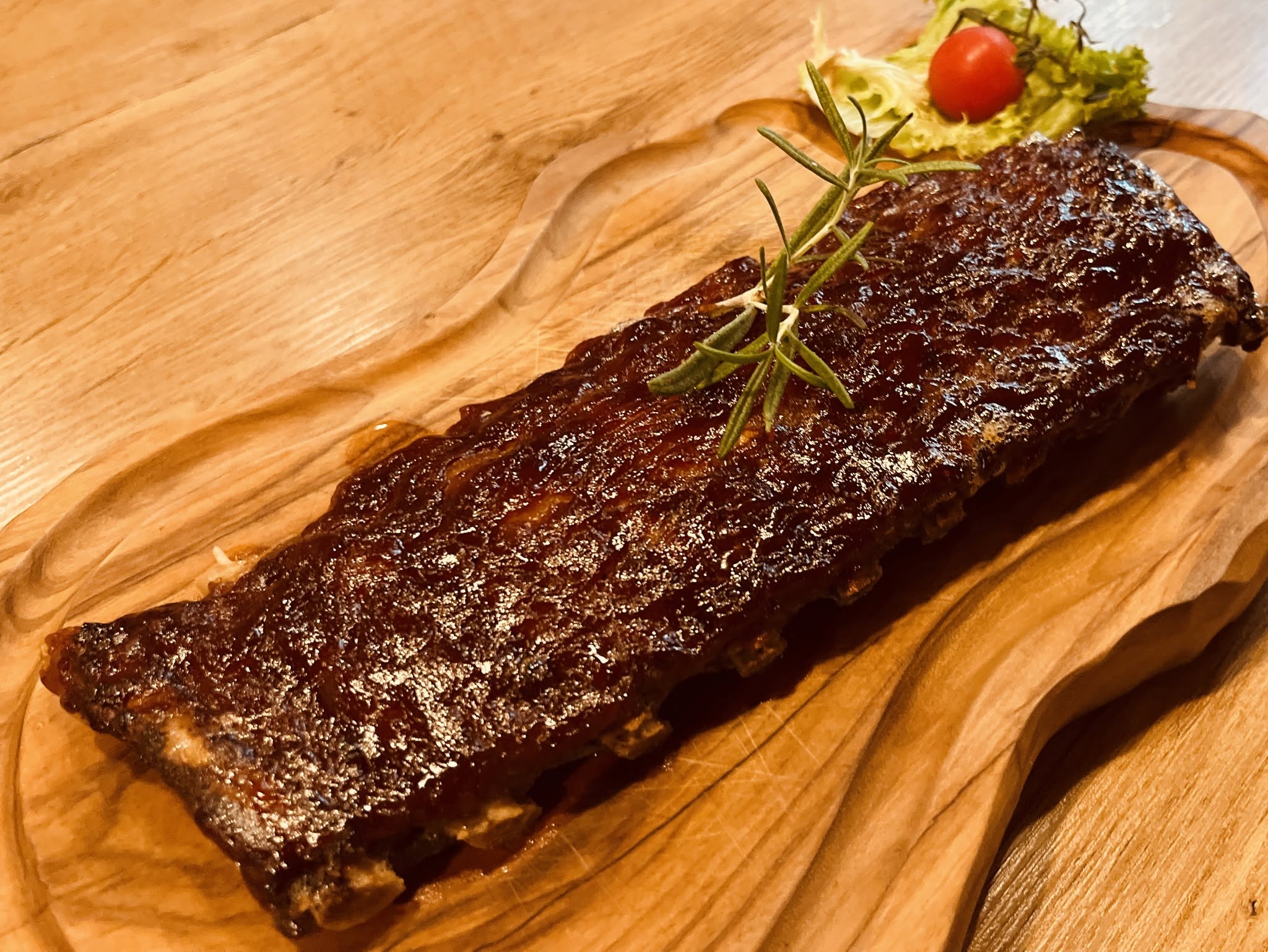 Spare Ribs mit BBQ-Sauce, Rosmarin und Tomate auf einem Holzbrett